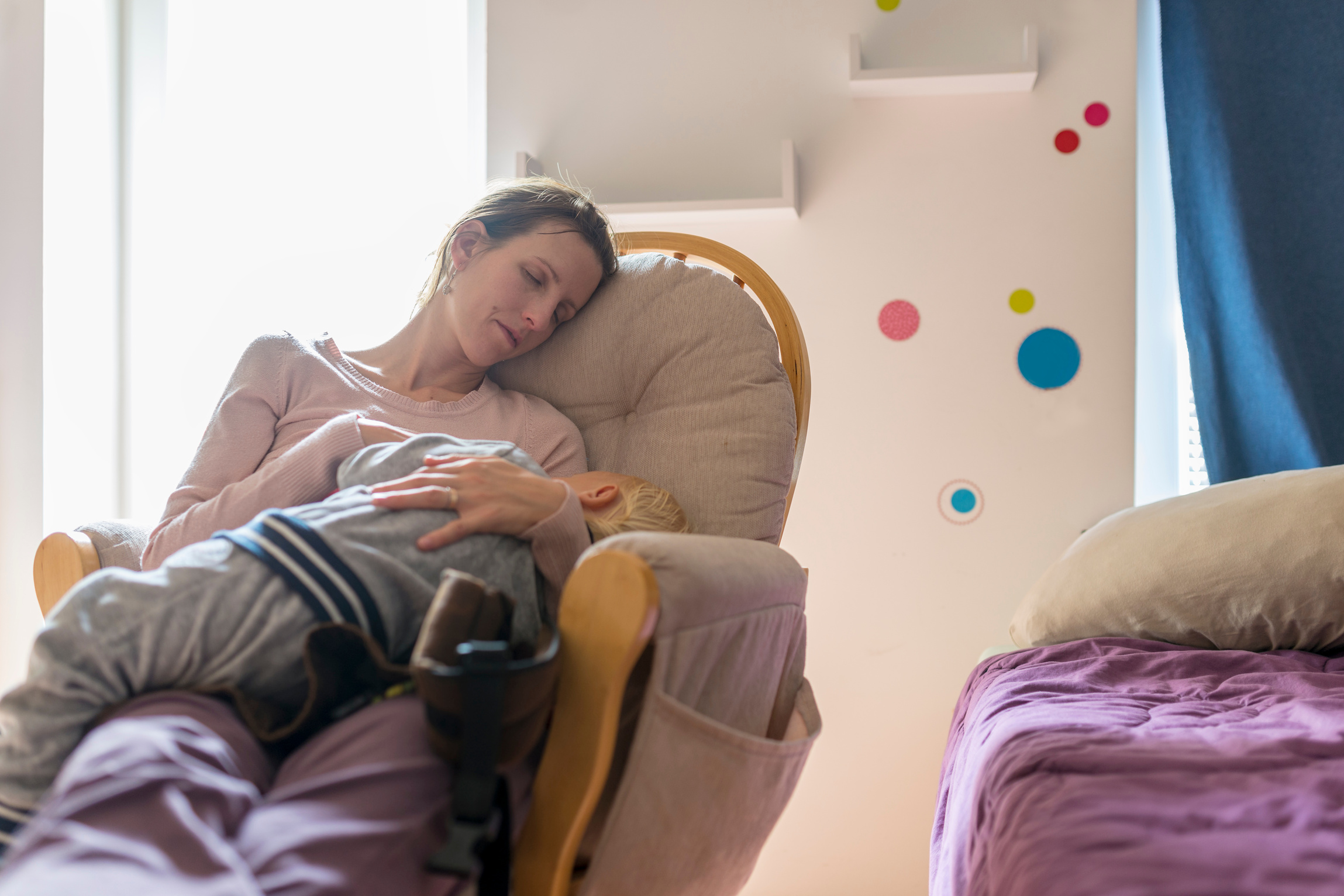 Tired Young Mother Resting on a Rocking Chair with Baby Sleeping